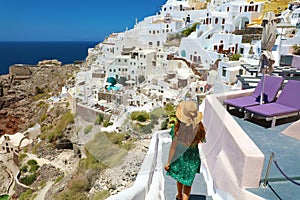 Young fashion woman with green dress and hat walking on stairs in Oia, Santorini. Female travel tourist on her summer vacations