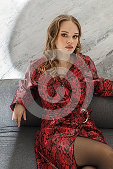 Young fashion woman in red leather coat on sofa