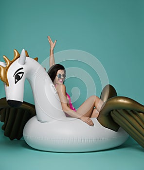 Young fashion woman relaxing with big inflatable unicorn pegasus float mattress in sexy pink bikini for swimming pool