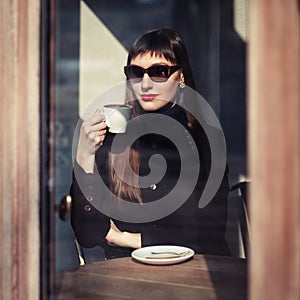 Young fashion woman sitting in cafe on the street with cup of cappuccino. Outdoors portrait in retro style