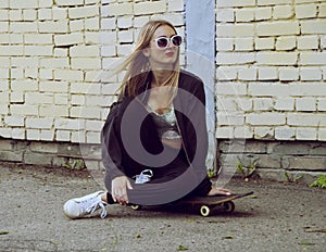 Young fashion woman sitting on skateboard. Girl in sunglasses with longboard on city streets