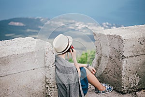 Young fashion woman sitting on a top of the mountain drinking tea with beautiful mountains and ocean view on the background