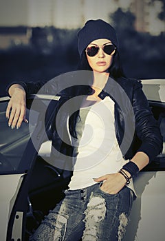 Young fashion woman in sunglasses leaning on her car