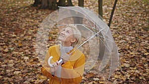 Young fashionable blond caucasian woman with transparent umbrela looking around in the park in autumn