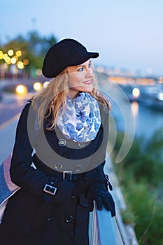 Young fashionable brunette woman in winter cap walking at evening in city