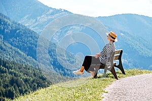 Young fashionable dressed female in straw hat sitting on a bench enjoying Santa Maddalena village view and stunning picturesque