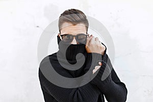 Young fashionable guy in black sunglasses vite and covers the fa photo