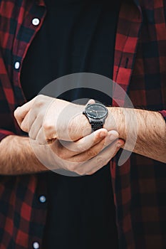 Young fashionable man wearing a red checked shirt and a black analog wrist watch. street style detail of