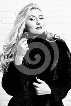Young fashionable pretty woman with beautiful long curly blonde hair in waist coat of black fur and fashion makeup