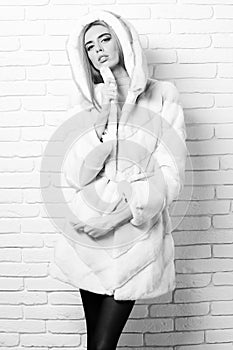 Young fashionable pretty woman or girl with beautiful long blonde hair in waist coat of white fur with hood and