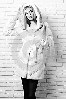 Young fashionable pretty woman or girl with beautiful long blonde hair in waist coat of white fur with hood and