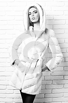 Young fashionable pretty woman or girl with beautiful long blonde hair in waist coat of white fur with hood and