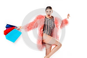 young fashionable sexy pretty girl in pink coat of fur with hood and fashion makeup holding colorful package in studio