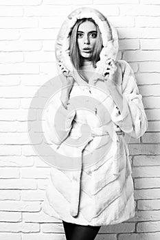 Young fashionable pretty woman or girl with beautiful long blonde hair in waist coat of white fur with hood and