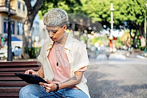 Young fashionable student girl working on her digital tablet or watching something on social media outdoor.Modern woman in short
