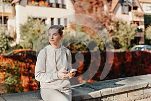 Young Fashionable Teenage Girl With Smartphone In Europian Park In Autumn Sitting At Smiling. Trendy Young Woman In Fall