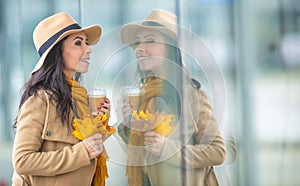 Young fashionable woman is doing window shopping holding takeaway coffee and autumn leaves