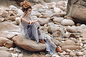 Young fashionable woman sitting on the stone beach