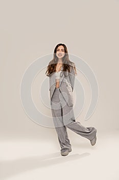 Young fashionable woman wearing grey females suit, standing and posing on light gray studio background. Smiling student