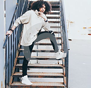 Young fashionably dressed man in a cool outfit posing on a metal staircase. Afro style hair. Streetstyle. Youth fashion.