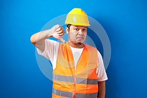 Young fat asian construction worker man wearing orange safety vest and helmet looking unhappy and angry