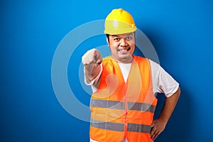 Young fat asian construction worker man wearing safety helmet pointing forward