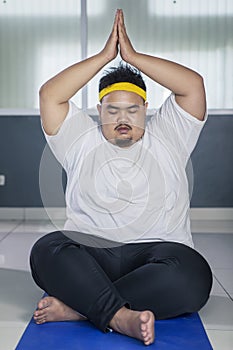 Young fat man doing yoga exercise on the mat