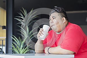 Young fat man drinking a glass of cola in the cafe