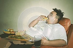 Young fat man eats burger with gluttony expression photo