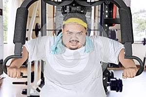 Young fat man exercising with a fitness machine