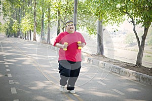 Young fat man jogging with dumbbells on the road