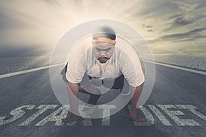 Young fat man kneeling above text of start diet