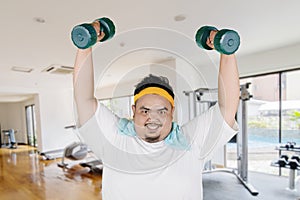 Young fat man lift dumbbells in the gym center