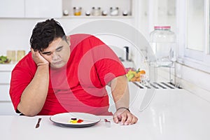 Young fat man looks bored to eat salad