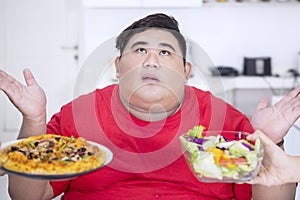 Young fat man looks doubtful to choose foods