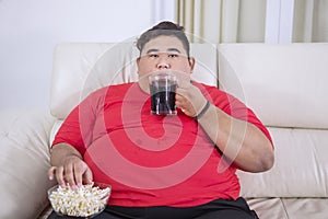 Young fat man watching TV with cola and popcorn