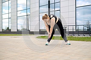 Young fat overweight woman does sports by stretching and bending forward on city streets