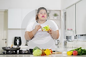 Young fat woman eats tasty salad in the kitchen