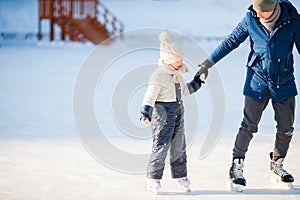 Young father and adorable little girl have fun on skating rink outdoors