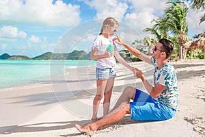 Young father applying sun cream to daughter nose on the beach. Sun protection
