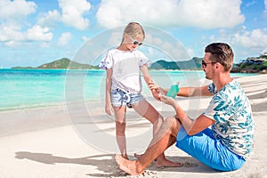 Young father applying sun cream to daughter nose on the beach. Sun protection