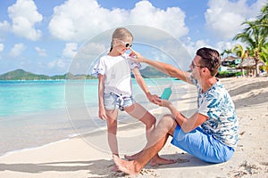 Young father applying sun cream to daughter nose on the beach. Sun protection