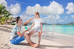 Young father applying sun cream to daughter nose on the beach. Sun protection