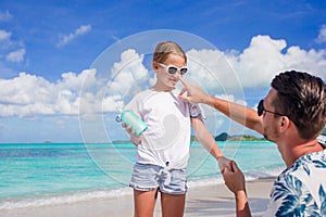 Young father applying sun cream to daughter nose on the beach. Sun protection