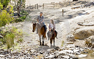 Young father as horse instructor of young teen daughter riding little pony wearing cowgirl hat