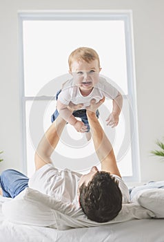 young father with a baby boy having fun with his son close to a window on bed