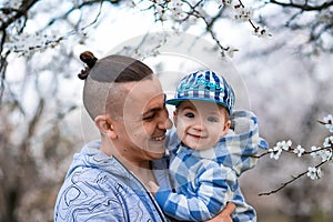 Young father and child son together, hugging and laughing in a Flowering apricot garden. Family outdoors lifestyle