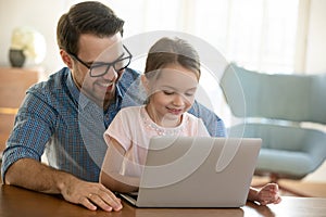 Young father cuddling small preschool daughter, using computer.