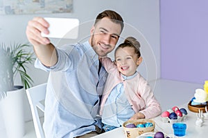 Young father and daughter taking selfie while painting eggs