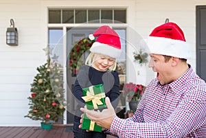 Young Father and Daughter Wearing Santa Hats On Front Porch of House With Christmas Decorations